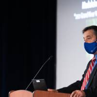 Speaker wearing mask welcoming everyone to the event.